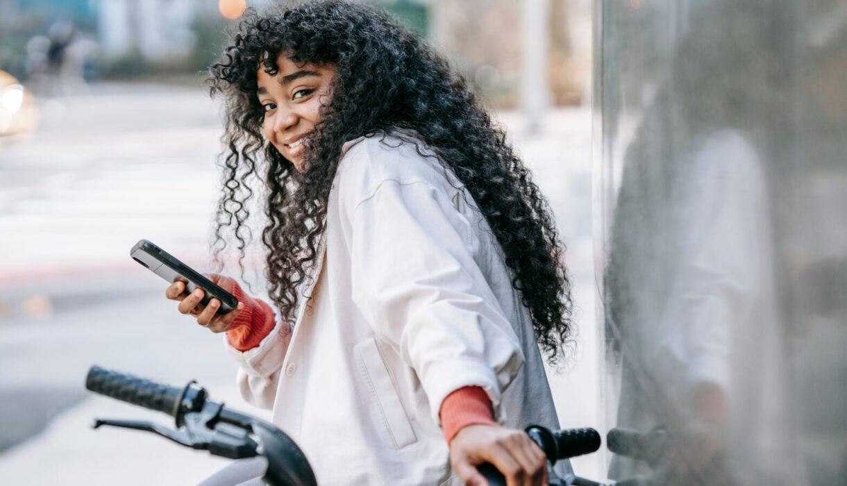 Woman smiling while checking her phone on a sunny city street
