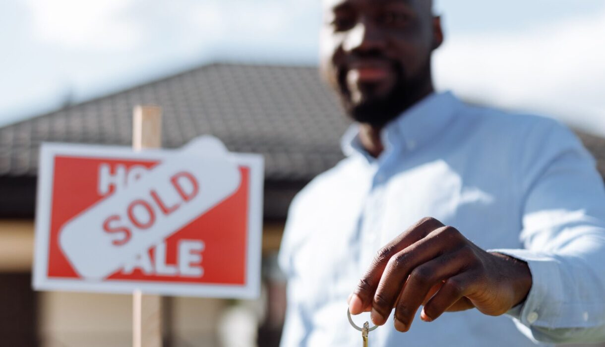 Smiling real estate agent holding a house key and sold sign outdoors