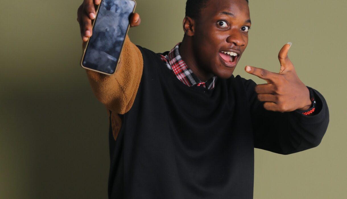 Smiling African man pointing at a smartphone in a studio portrait