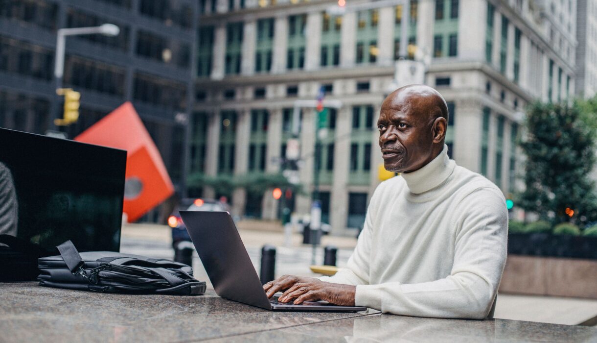 Mature Black businessman focused on his laptop working in a bustling downtown cityscape