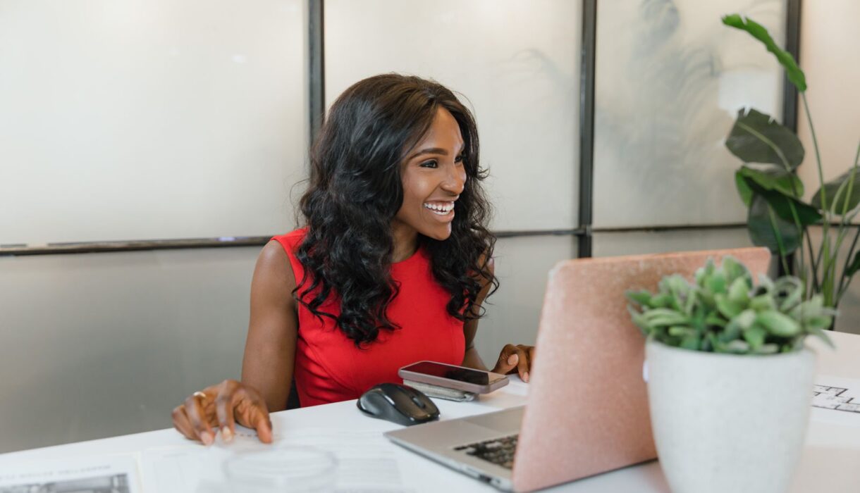 Smiling woman using a smartphone and laptop at her office desk