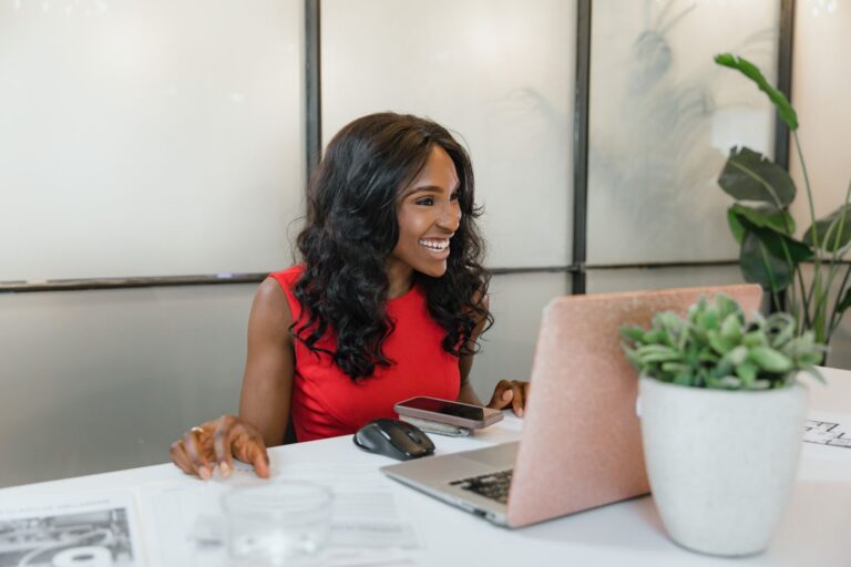 Smiling woman using a smartphone and laptop at her office desk